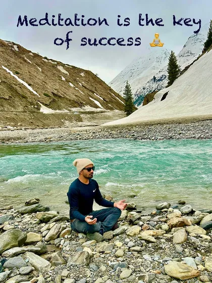 Finding the key to success in meditation, seated by a turquoise river with snow-capped mountains in the distance.