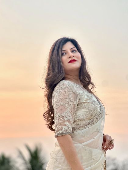 A stunning sunset portrait of Savaniee. She looks ethereal in a white sequined saree, with bold red lips and soft, romantic waves in her hair.