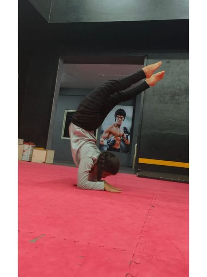 Practicing a forearm stand against the wall, with the iconic Bruce Lee poster in the background for inspiration.