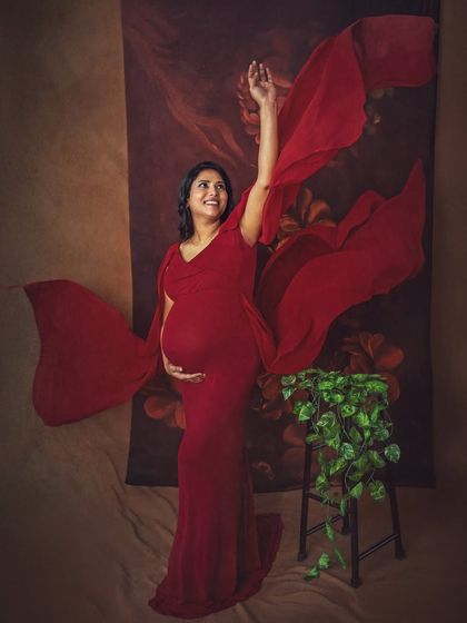 A joyful and dynamic shot with the red gown's fabric flowing in the air. This adds a sense of movement and celebration to the maternity portrait, capturing the mother's happy spirit.