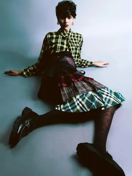 A playful, seated pose from 'My Flatmate's Wardrobe.' The mix of plaid patterns and chunky shoes captures a spunky, eclectic spirit.