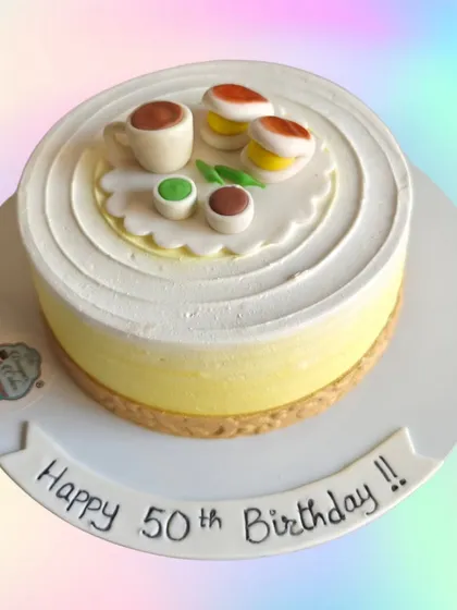 A minimalist cake with a topper of edible macarons and a cup of tea. A simple and charming design for a 50th birthday.