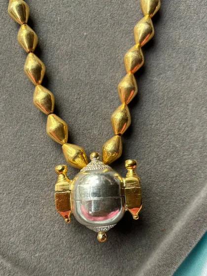 A minimalist yet striking dual-tone necklace. This piece features a simple, polished silver orb-like pendant with gold-plated accents, strung on a classic gold-beaded chain.