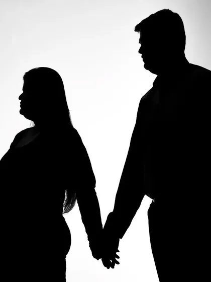 A strong and simple silhouette of a couple holding hands. The focus is entirely on their connection and the shape of the mom-to-be.