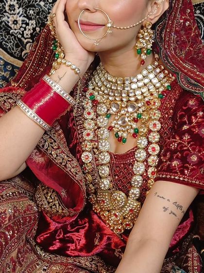 A close-up of a bride's heavy, layered jewellery set with red and white stones. The tattoo on her arm adds a modern touch to the traditional look.