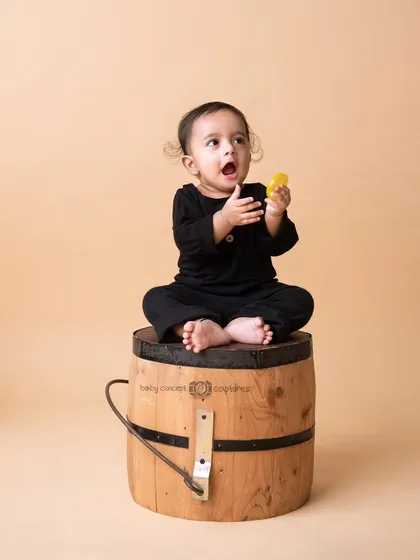 A full-body shot of a baby sitting on a barrel, capturing a moment of surprise and curiosity.
