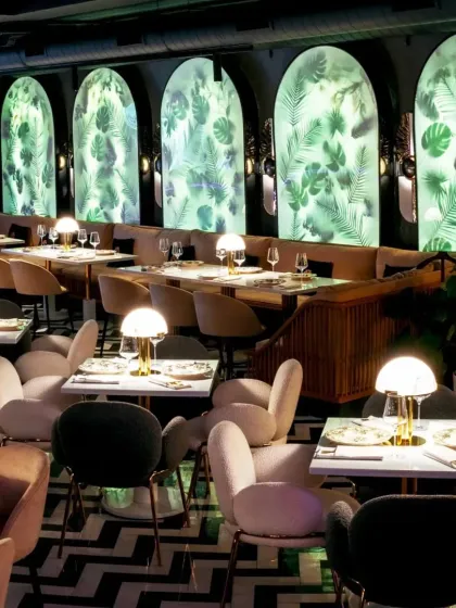 An overall view of the restaurant, highlighting the contrast between the dark, patterned floor and the glowing botanical wall panels. The layout is designed to feel both lively and intimate.