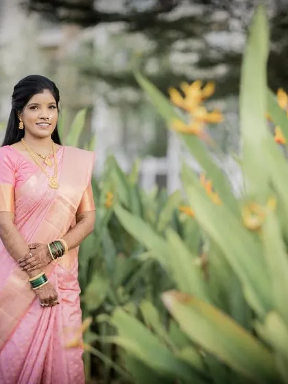 The bride-to-be poses gracefully in a garden, her pink saree complementing the surrounding greenery.
