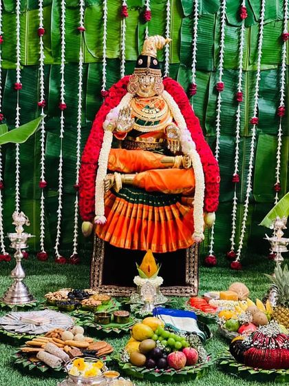 A wide view of the pooja setup on a bed of green, with the Goddess in her bright orange and green saree as the focal point.