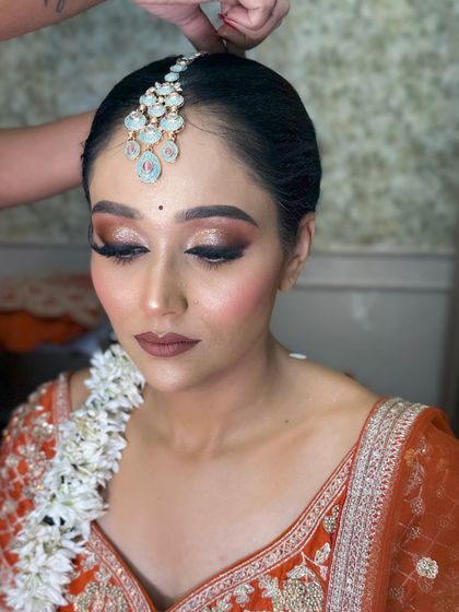 A close-up of the bride in the orange lehenga, showing her beautiful eye makeup and the floral gajra in her hair.