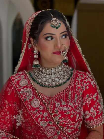 A side profile of our bride, showcasing the detailed eye makeup and the intricate design of her nath and emerald jewelry set against her red bridal attire.