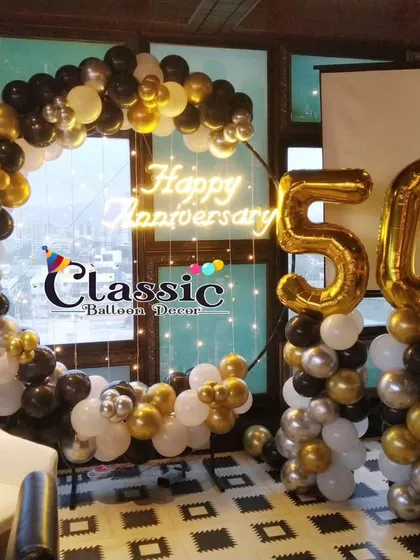 We set up this classic 50th anniversary decoration on a rooftop. The design includes a balloon ring in black, white, and gold, a 'Happy Anniversary' neon sign, and large '50' foil balloon numbers.