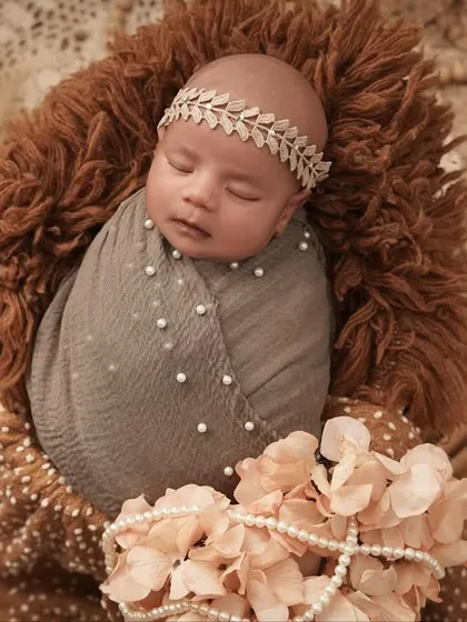 An overhead shot of a sleeping newborn, styled with a delicate leaf-patterned headband and surrounded by dried palms and flowers. This setup has a lovely, natural, and bohemian vibe.