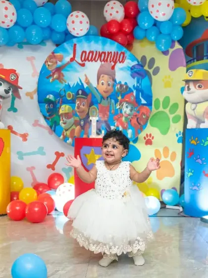 The birthday girl stands in her beautiful white dress, ready to dance in front of a colorful Paw Patrol themed backdrop.