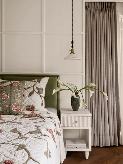 A detail of the guest bedroom in "Apartment 222," showing the floral bedspread and the simple, elegant bedside table. The pendant light adds a touch of vintage charm to the modern space.