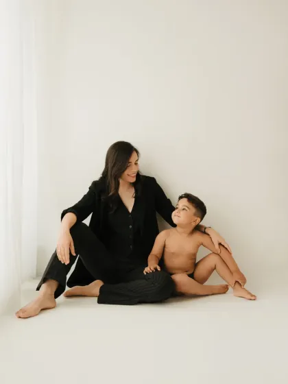 A full-length portrait of a mother and son sitting together. The minimalist setting and their comfortable interaction create a timeless image.