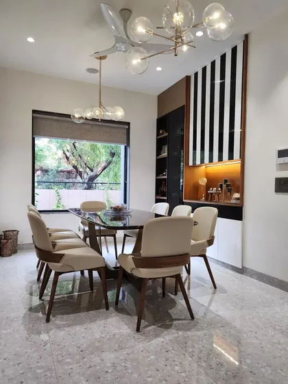 The dining area of a modern luxury villa, where large windows frame the garden view, bringing the outdoors in. This space balances elegant interior design, featuring terrazzo flooring and contemporary lighting, with a constant connection to natural light and greenery.