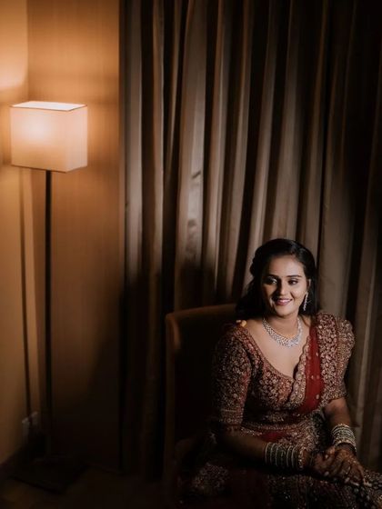 A happy bridal portrait in a warmly lit room. The bride's smile and her elegant reception lehenga are the focus of this classic shot.
