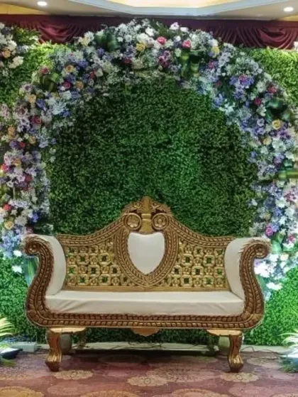 A beautiful baby shower stage with a green foliage wall and a floral arch in shades of purple and white. The elegant sofa and stand-up lights complete this modern yet traditional look.