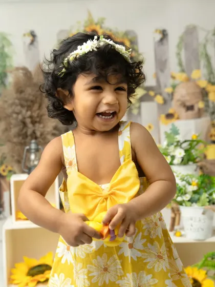 A bright, joyful laugh in a sunflower-themed setup. This little girl's happiness is contagious in her sunny yellow dress.