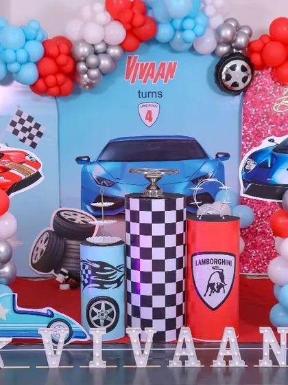 A high-energy race car themed party for a 4th birthday. The decor features a custom backdrop with sports cars, a fuel station prop, checkered flags, and a large light-up number '4', creating a perfect trackside experience.