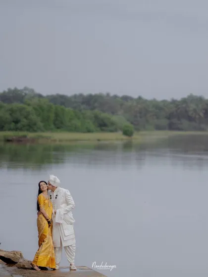 A romantic kiss by the water's edge. The serene landscape and the couple's intimate moment combine to create a breathtakingly beautiful photograph.