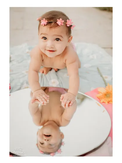 I love getting creative during my sessions. Using a mirror for this outdoor shot adds a unique, reflective element to this baby girl's first birthday portrait, capturing her sweet curiosity.
