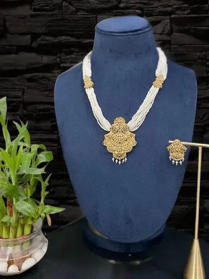 A beautiful Jadau necklace set featuring a large, intricately carved gold pendant and matching earrings, strung with multiple strands of pearls. This piece exudes a royal and vintage charm.