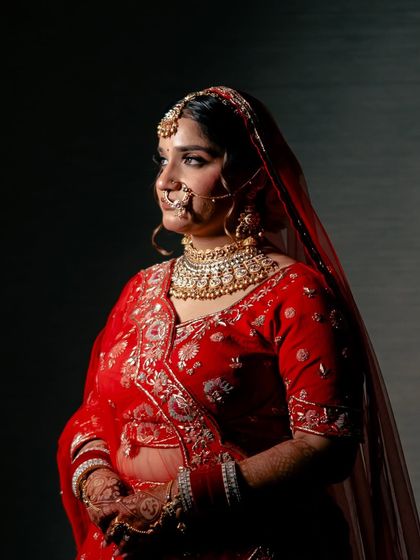 A classic portrait of a bride in a traditional red lehenga. The dramatic lighting creates a regal and timeless look.