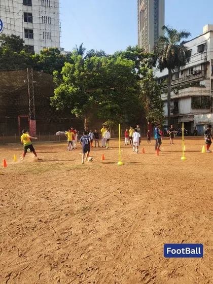 Football drills in progress at our Matunga sports camp. Young players are seen navigating a cone drill on a mud pitch, building agility and ball control skills.