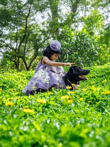 A little girl sits in a field of flowers, gently patting her black Labrador, Bagheera. This serene and beautiful image captures the quiet, loving moments that happen during a relaxed outdoor family session.