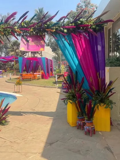 A vibrant poolside entrance for a "Phoolon ki Haldi" (Haldi of Flowers). The decor uses colorful drapes and tropical foliage to create a high-energy, festive atmosphere.
