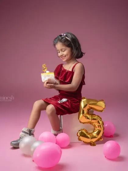 A sweet moment from a fifth birthday session, where the birthday girl holds a small cake with a number '5' candle. The simple pink backdrop keeps the focus on her happy expression.