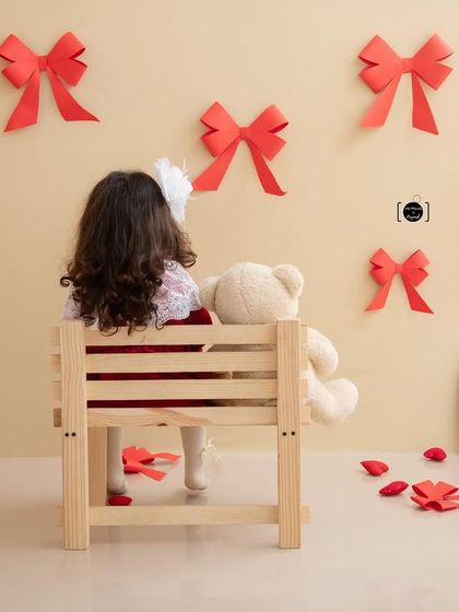 A girl and her bear, sitting on a bench and enjoying the view of red bows and hearts. A sweet, story-like image.