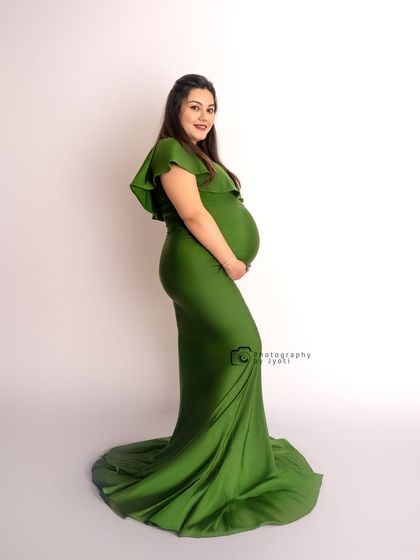 A simple and elegant profile shot in a green gown against a clean white background, highlighting the beautiful silhouette of pregnancy.