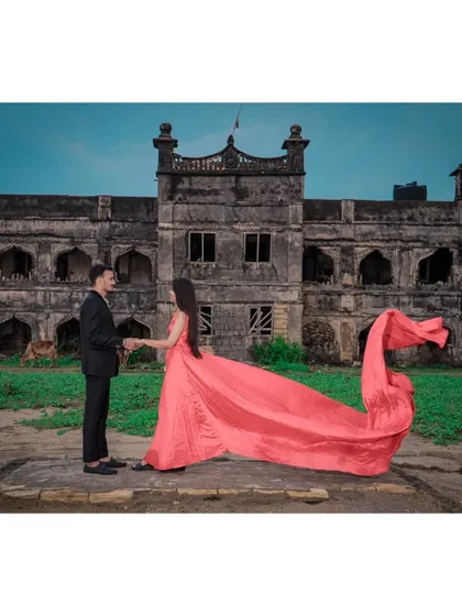 A couple shares a moment in front of a magnificent, old fort, with the bride's dramatic pink gown adding a splash of colour to the historic scene.