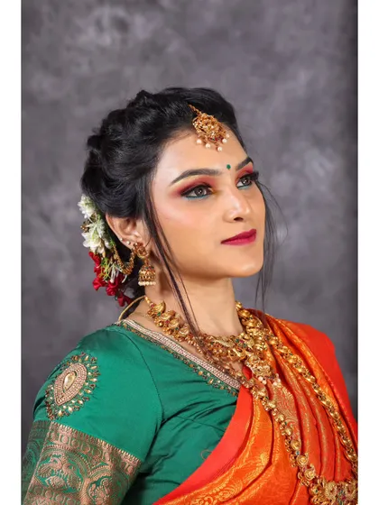 A three-quarter profile shot of the model, showcasing the elegant drape of the orange saree and the contrast with the green blouse.