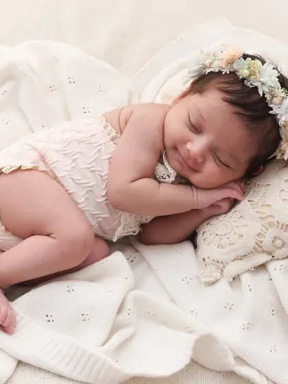 Sweet dreams, little one. A floral headband and a soft, lacey outfit create a delicate and angelic look for this newborn princess. The focus is on her peaceful sleep and cherubic features.