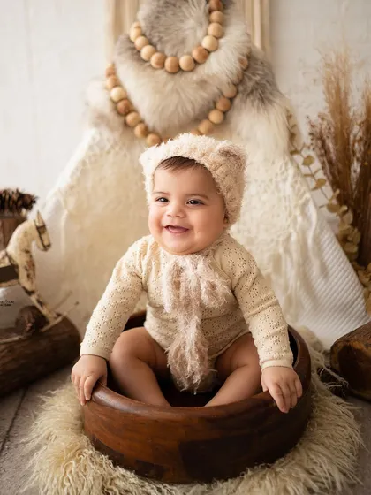 A happy six-month-old in a cute bear bonnet, part of a rustic woodland themed session.