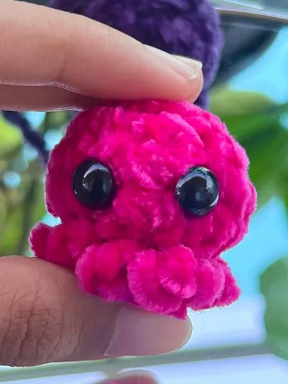 A close up of the mini octopus keychain in a vibrant hot pink. The soft, fluffy yarn and big eyes make it extra cute.