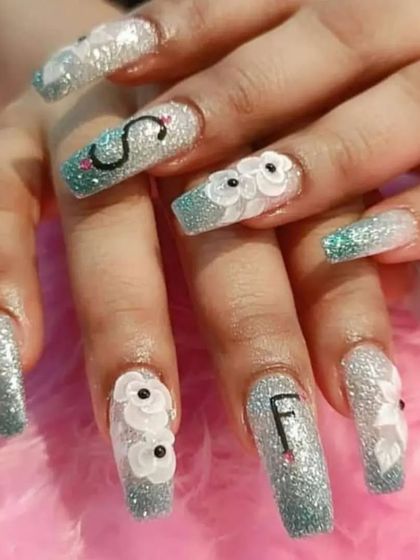 We can personalize your nails with initials or custom designs. This set features long, glittery extensions with 3D flowers and the letters 'S' and 'F'.