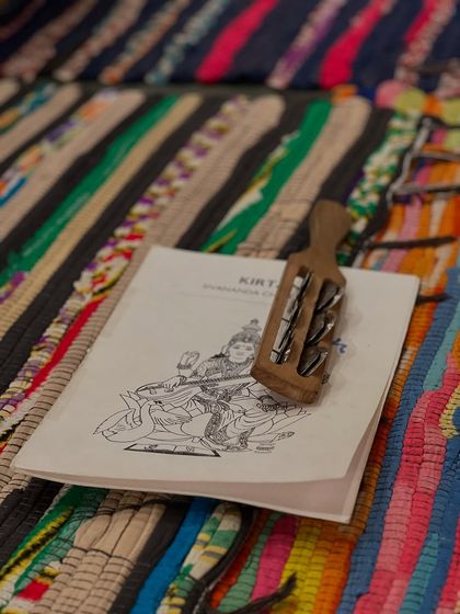 A kirtan booklet and a kartal, a traditional percussion instrument, rest on a colorful mat. Chanting and devotional music are an important part of our retreats, helping to open the heart and quiet the mind.