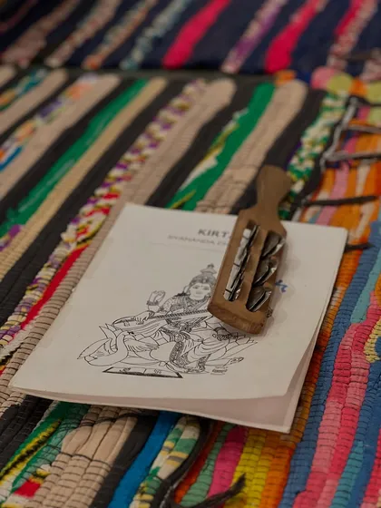 A kirtan book and kartal (hand cymbals) resting on a colorful mat. Chanting and kirtan are an important part of our satsangs, using sound to elevate the spirit.
