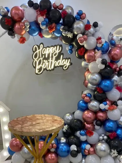 A vibrant 30th birthday setup with a multi-colored balloon arch, disco balls, and large marquee numbers.