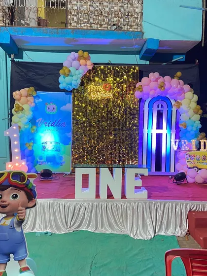 The main stage for a Cocomelon first birthday party. It includes a golden shimmer wall, large 'ONE' marquee letters, and multiple character cutouts.
