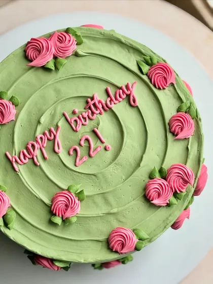An overhead view of the sage green cake, showing the swirl pattern and the placement of the pink rosettes.