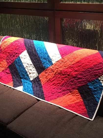 A modern, abstract quilt in bright colors, draped on a sofa.