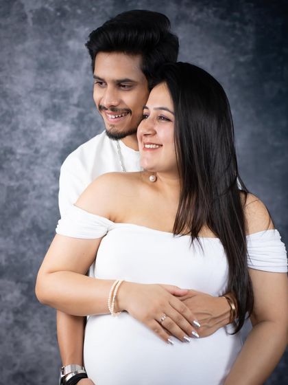 A happy and relaxed studio portrait. This couple, dressed in white, shares a smile against a classic grey backdrop, capturing their easy chemistry.