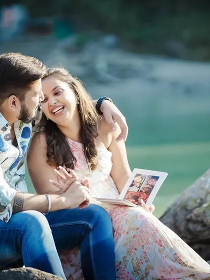 A fun, interactive moment during a riverside pre-wedding shoot, where the couple looks at a photo album together.