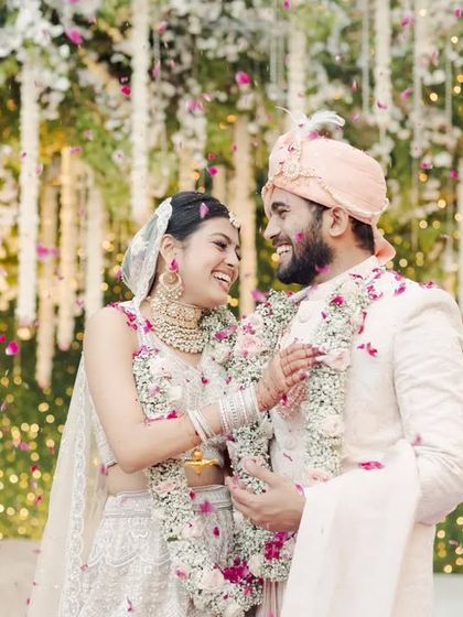 A happy portrait of the newly married couple. The soft textures of the hanging floral backdrop create a dreamy and romantic setting for their first photos together.